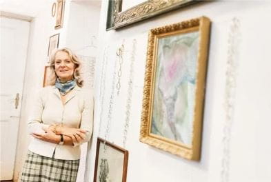 an art collector woman standing in front of a framed work of art hanging on the wall