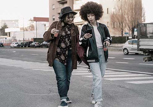 two young black women walking down the street looking at phone and smiling