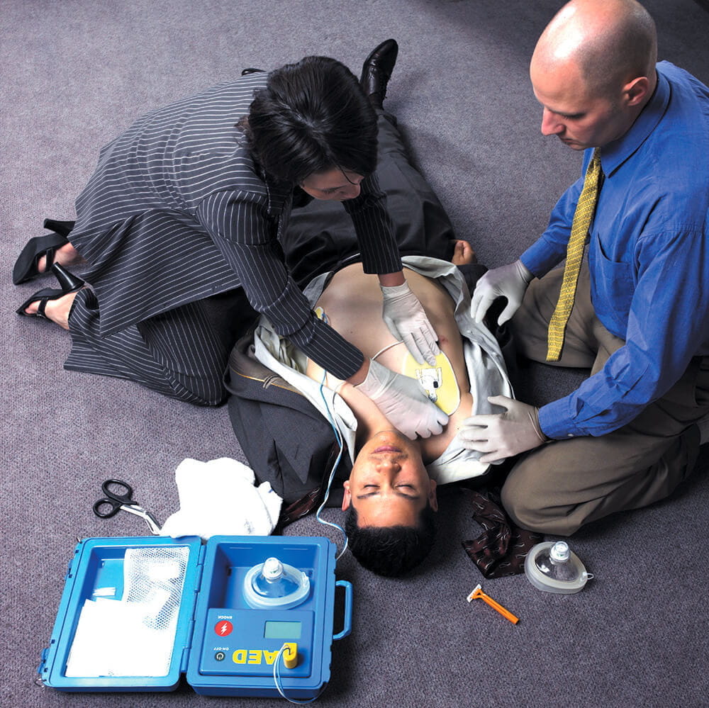 business woman using AED on man on office floor
