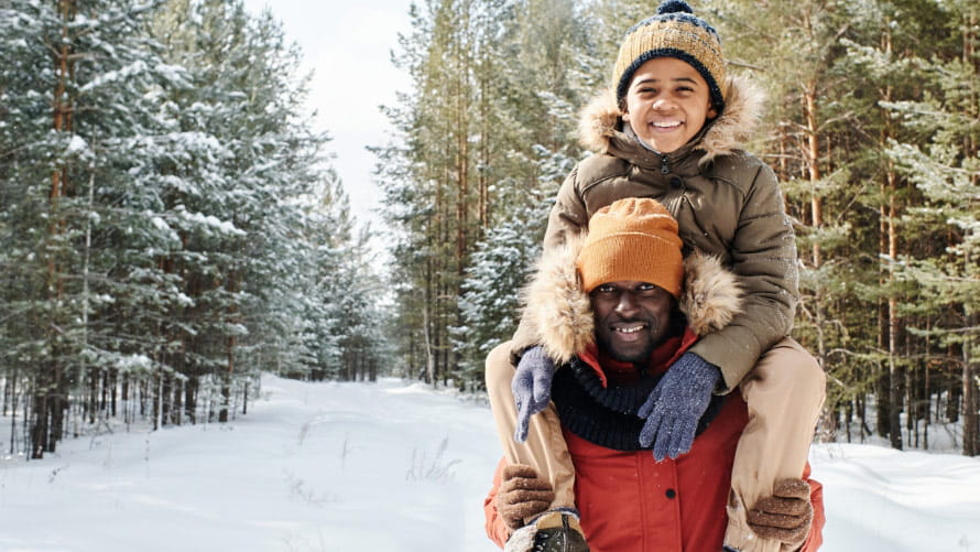 Child on father's shoulders in a snowy wooded area