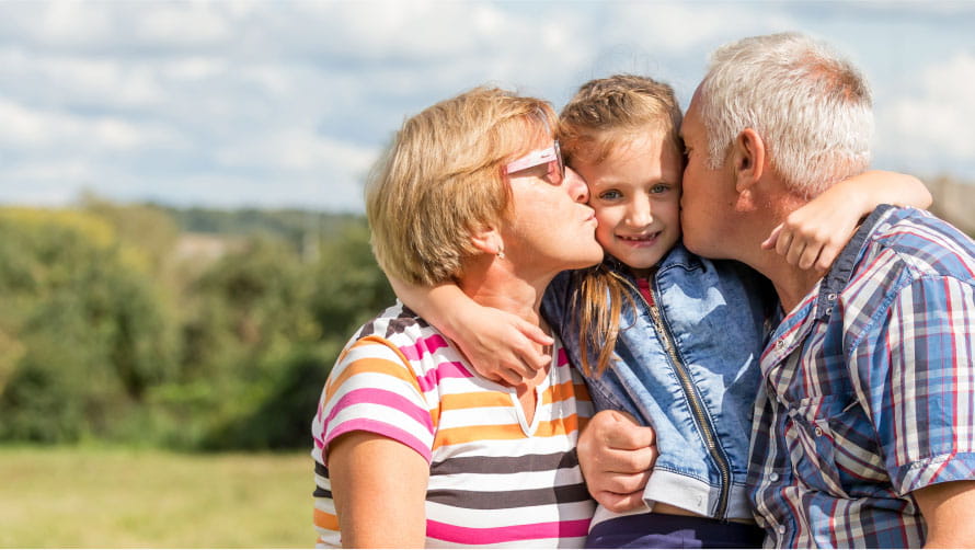 Granddaughter being held by grandparents while they kiss either cheek