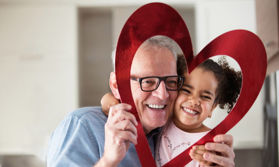 Man and a young girl smiling while holding a cutout of a red heart and peering through the middle