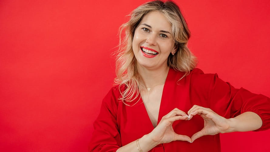 woman in front of red background with heart hands