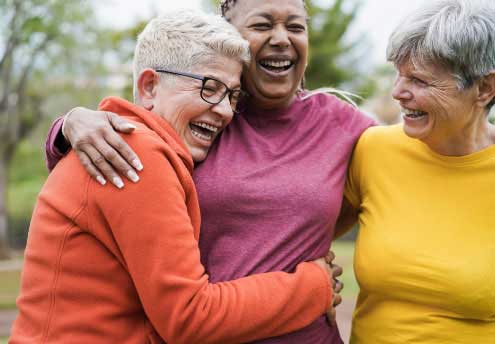 three middle aged women laughing and hugging