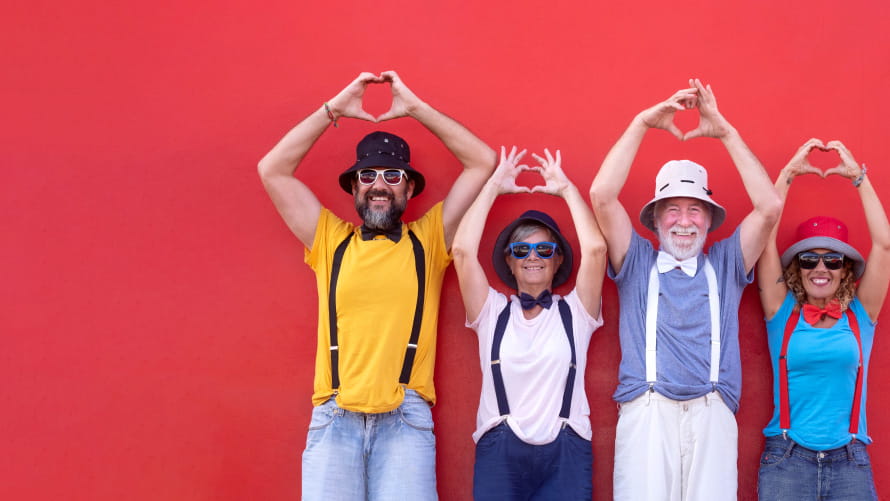 Four people in front of red wall holding their hands above their head making the shape of a heart
