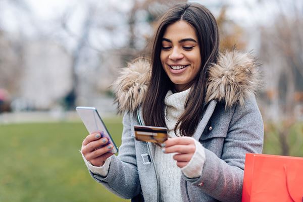 happy young woman uses credit card to donate on phone outdoors happy young woman uses credit card to donate on phone outdoors