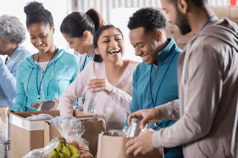 young people smiling while volunteering and loading bags with groceries