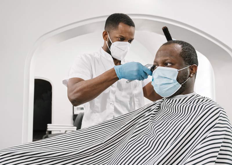 customer in barber shop getting hair cut. barber and custom are wearing protective masks.