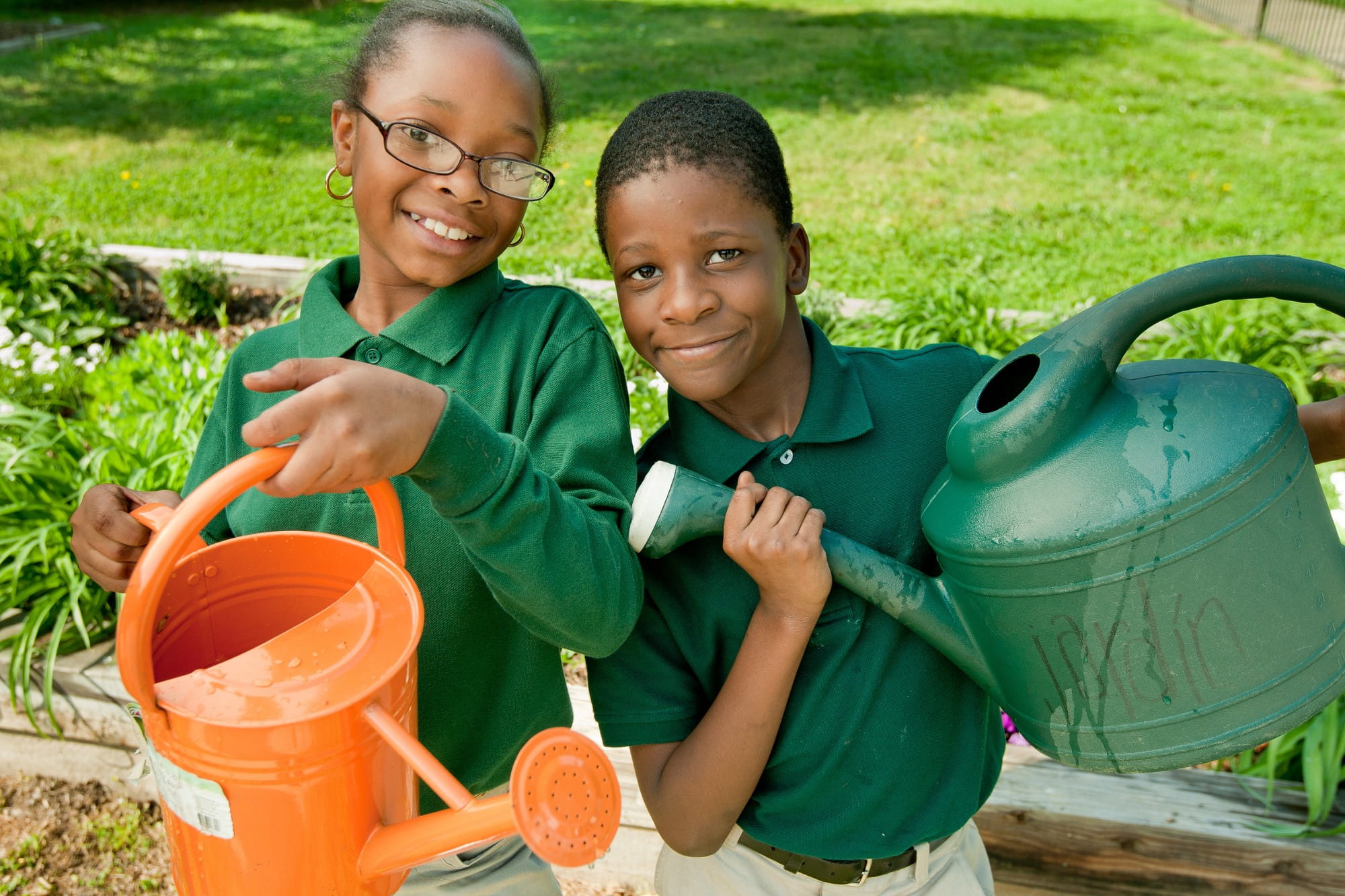 Two students holding watering cans as they participate in school garden program