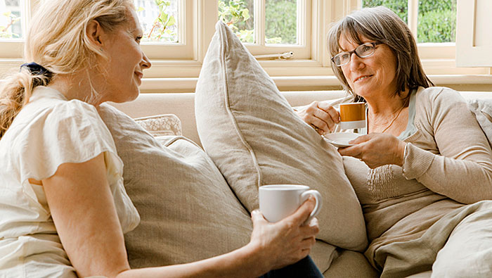 Two mature women talking and drinking coffee on a sofa