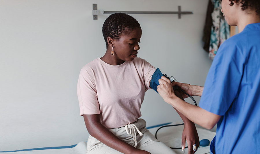 nurse taking young woman's blood pressure reading in doctor's office