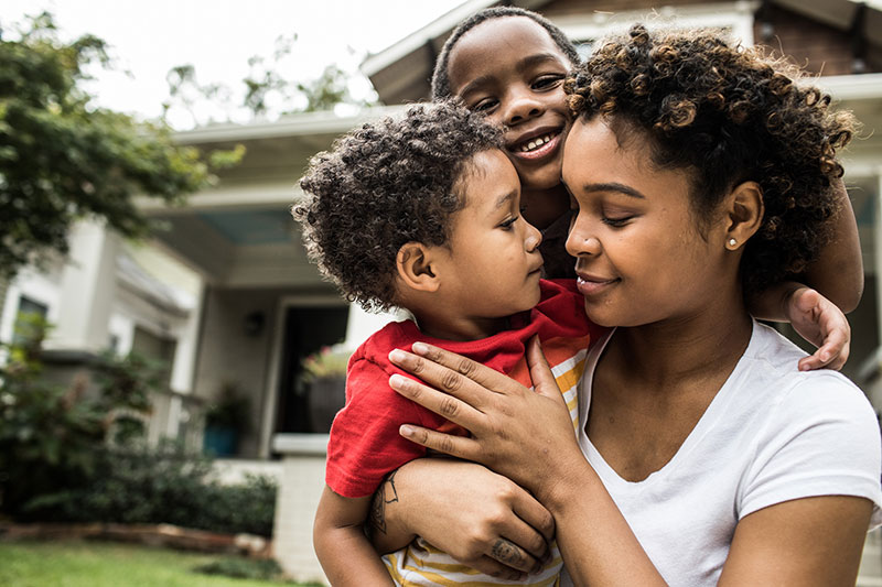 Mom and sons hugging outdoors GettyImages-1182075825