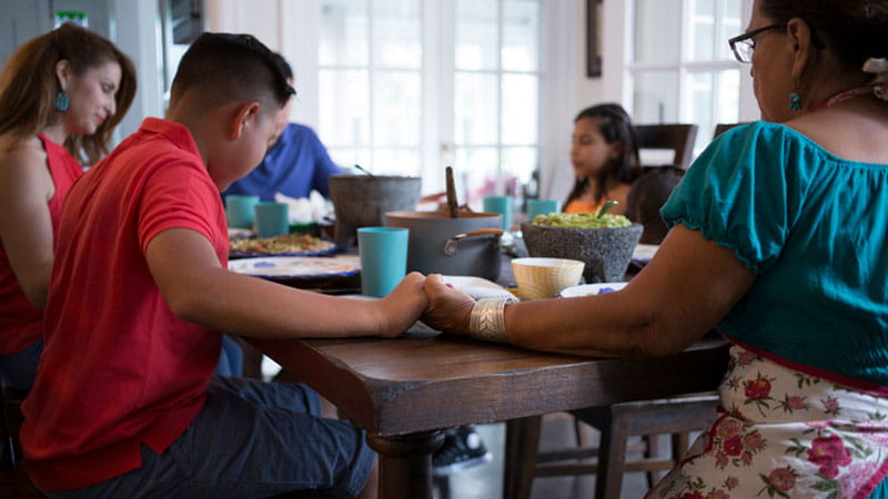 Family saying grace before a meal at a dining table