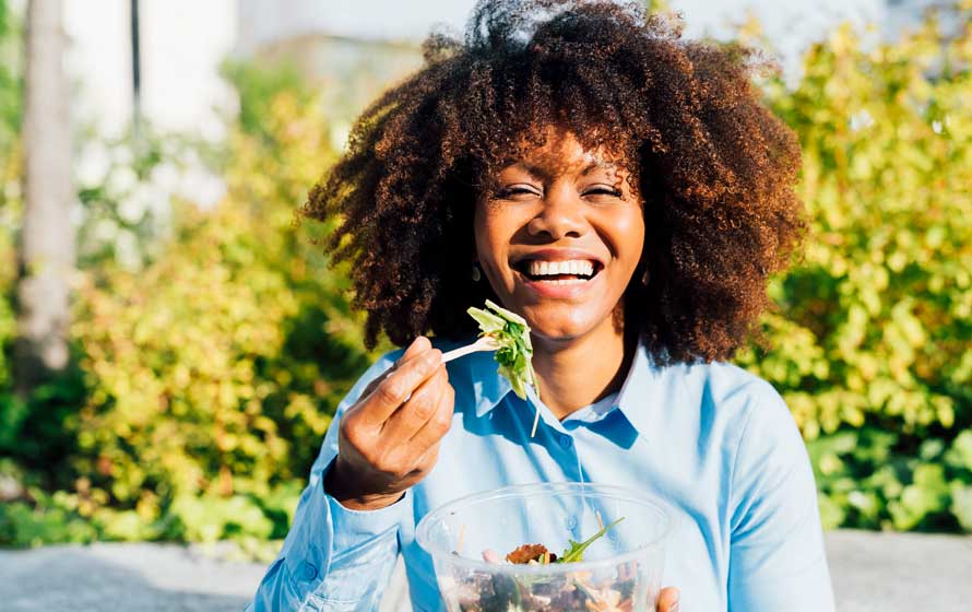 Happy businesswoman eating salad on sunny day