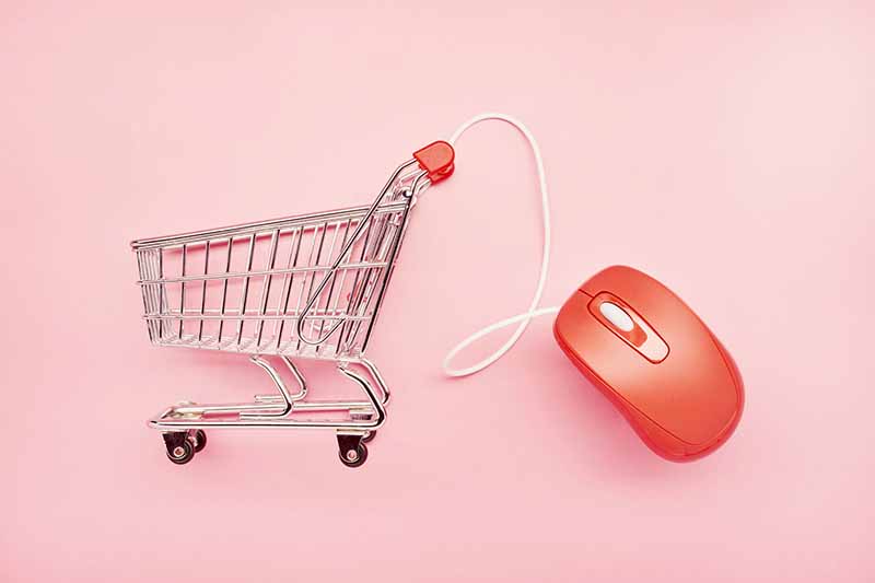 still life of a small shopping cart and red computer mouse on pink background, online shopping