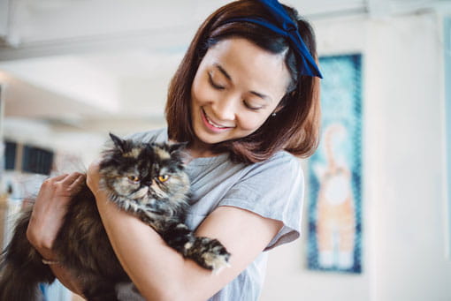 Young lady holding a fluffy cat in her arms joyfully.