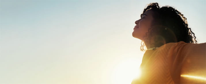 Young woman standing outside in the sun with arms outstretched.