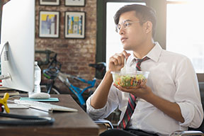 Young man eating salad at desk
