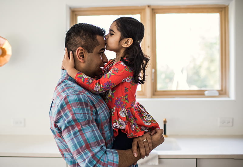 daughter kissing fathers forehead at home