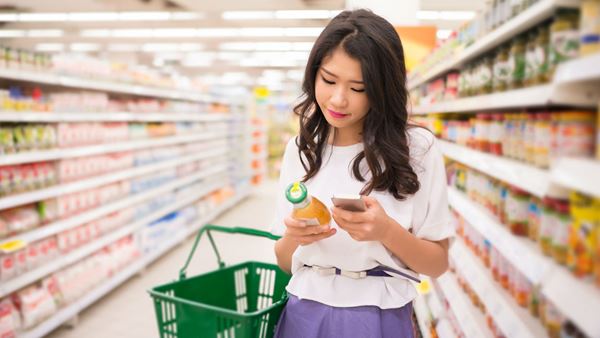 Asian Woman looking up ingredients on label using mobile phone