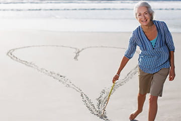 woman at beach drawing a heart shape in the sand with a stick