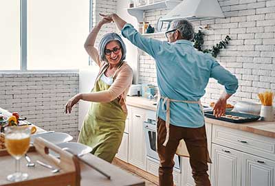 happy senior couple dancing while cooking at home