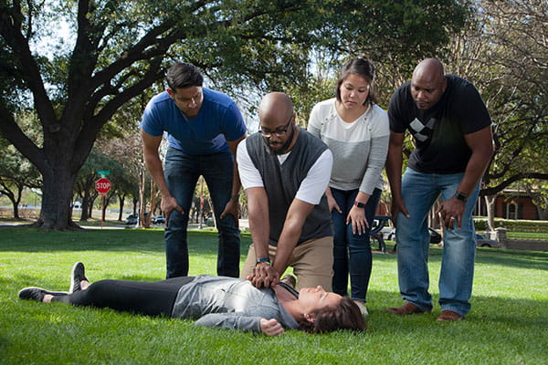 man performs CPR on woman in a park with onlookers