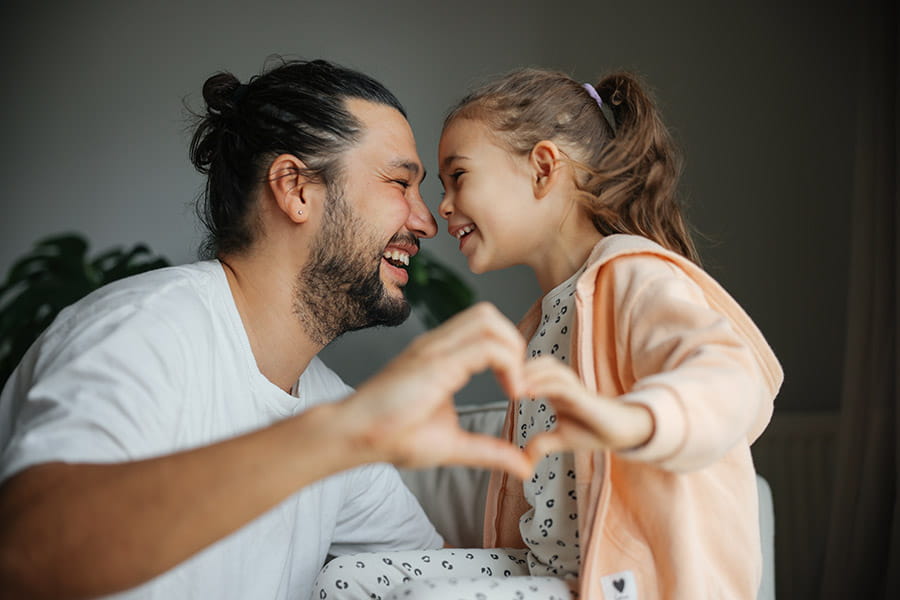 Smiling father with young daughter in a living room making hand heart gesture