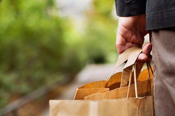 A man's hand carrying brown paper shopping bags while walking outdoors