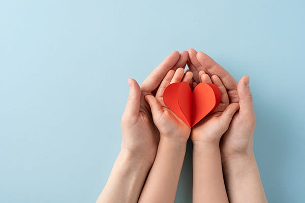 Adult and child nested hands holding a red paper heart