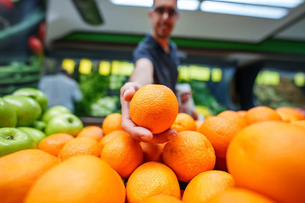 Selective focus on oranges in a produce section and a man in the background is choosing one