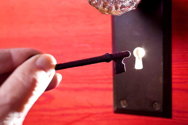 A skeleton key in front of an antique glass door knob with light coming through the keyhole