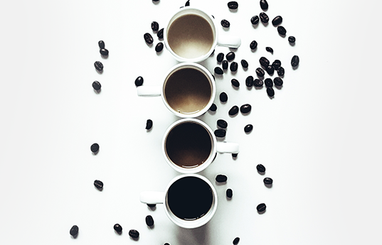 Four cups of coffee on white table with coffee beans scattered around