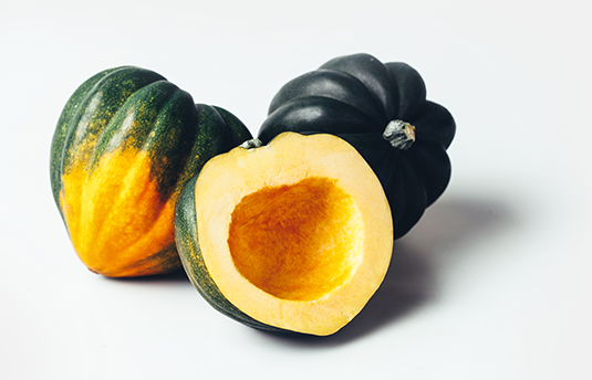 Two whole acorn squashes and one squash cut in half on white table