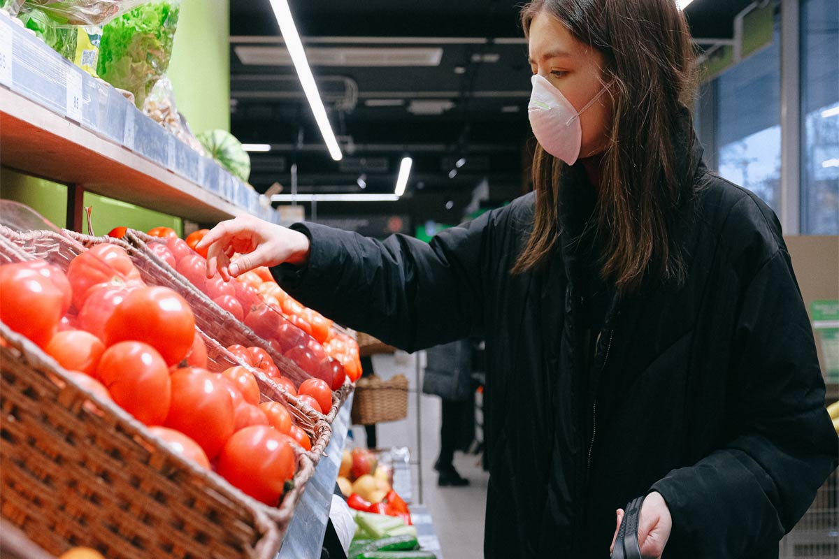 woman in mask shopping for fresh tomatoes at a market