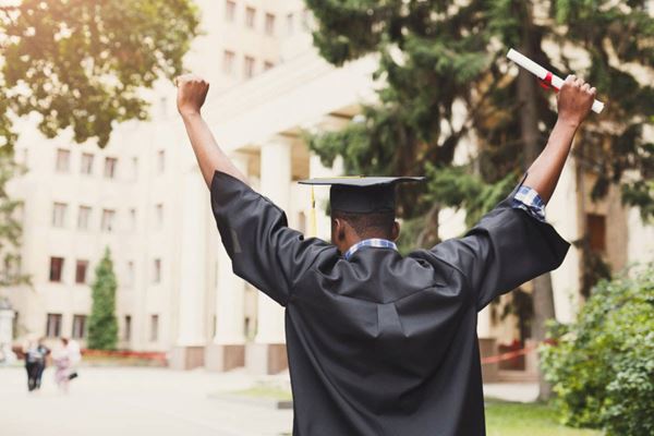 man in graduate cap and gown raising his arms in celebration
