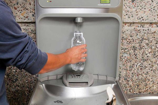person filling water bottle at water fountain