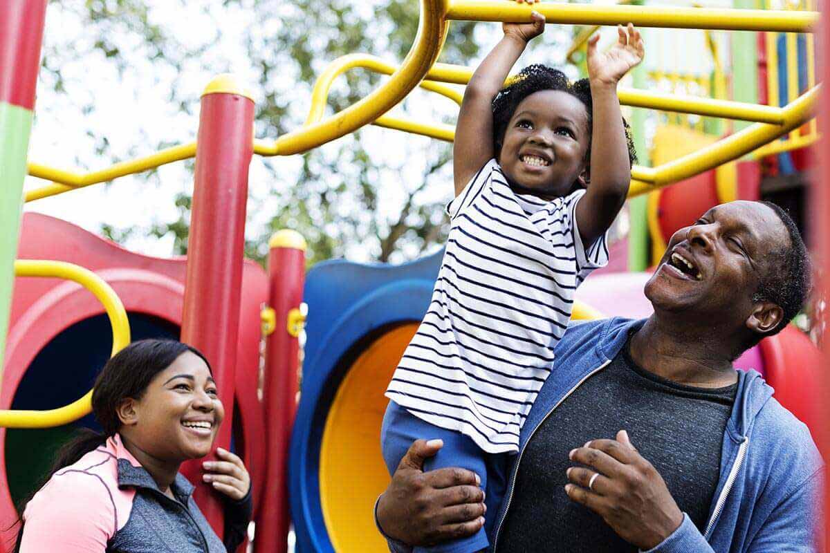 family with small girl playing at a play park