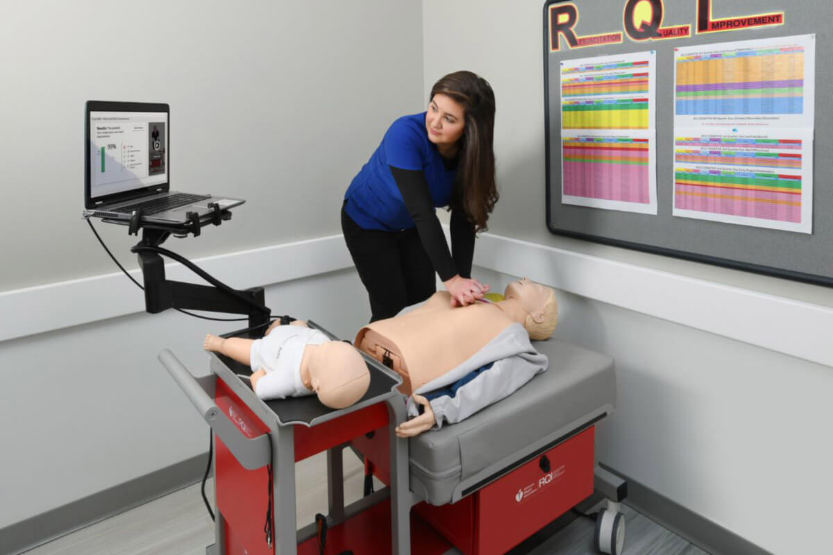woman practicing CPR on a dummy next to laptop