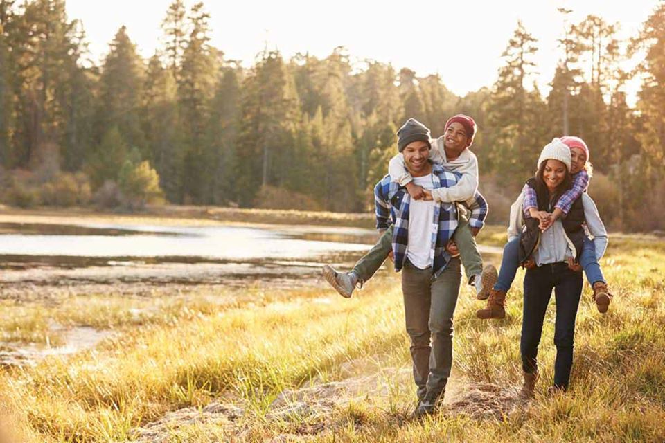 family hiking in woods with kids riding piggy back