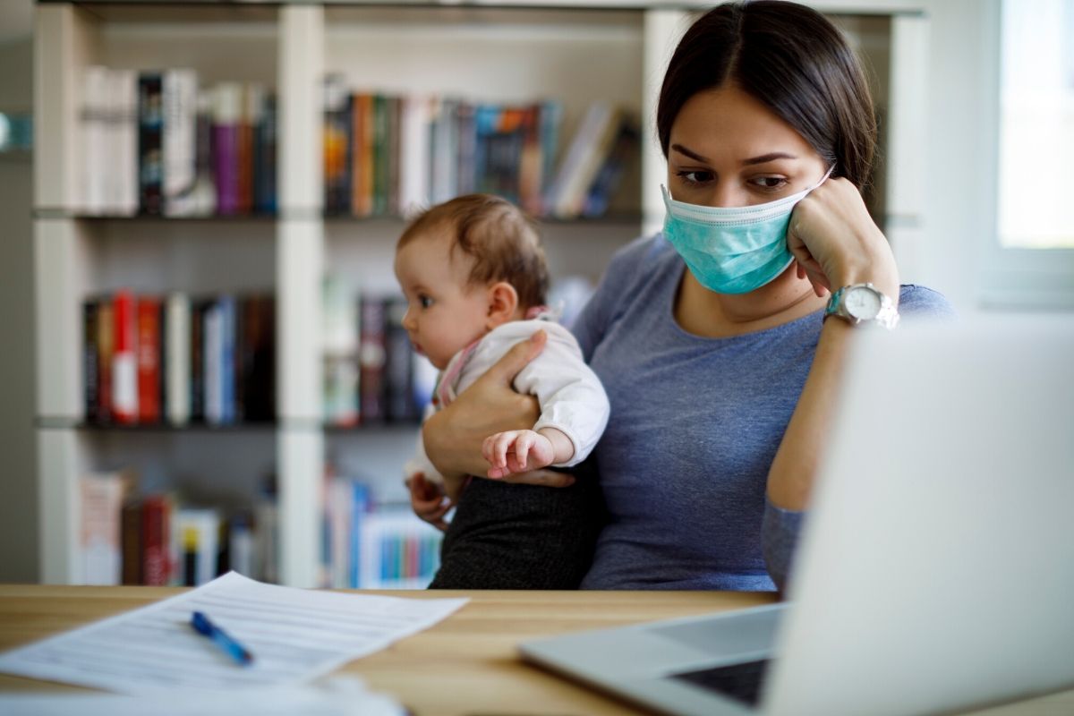 Mother wearing mask holding baby in front of computer