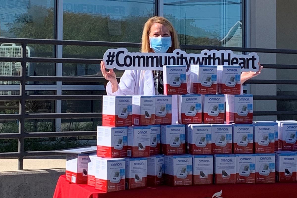 woman in mask holding #CommunitywithHeart sign by boxes of medical equipment