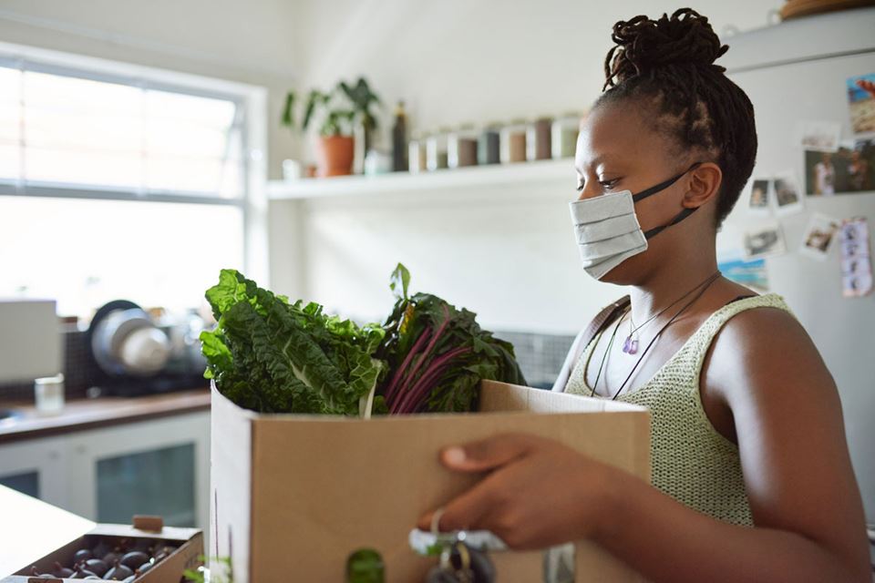 woman in mask holding box of fresh food