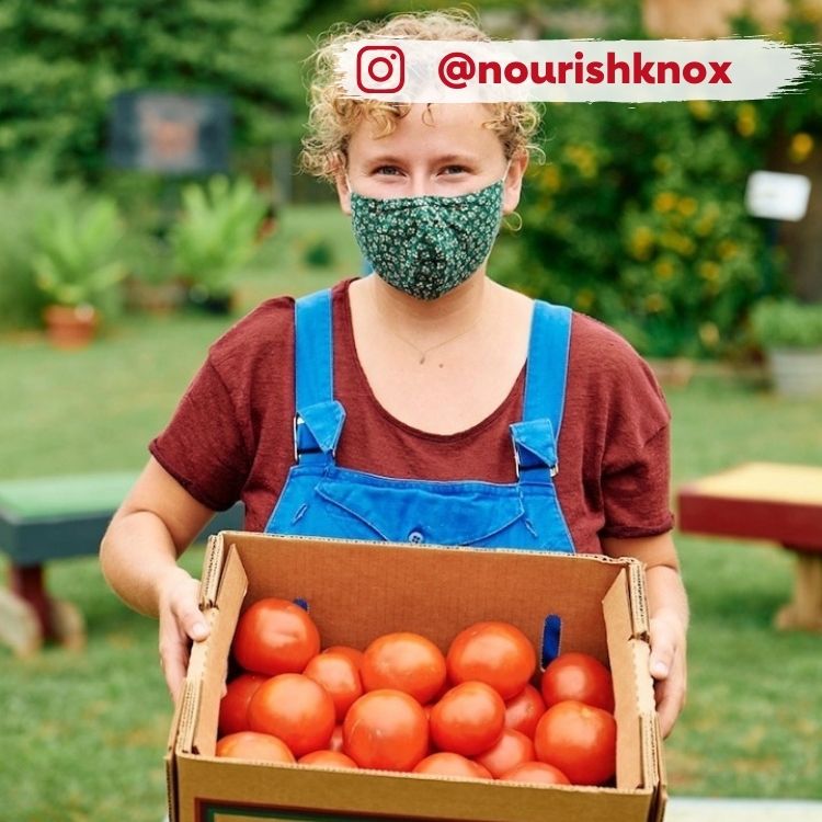 woman in mask holding box of tomatoes