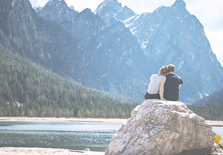 couple sitting on large rock overlooking lake and mountains