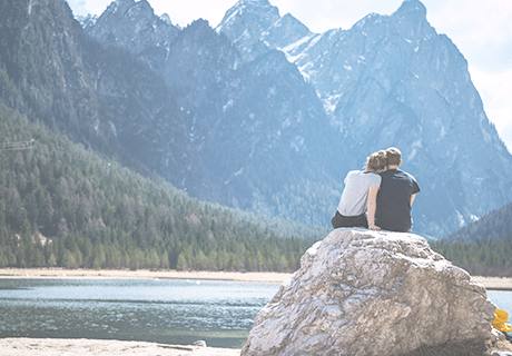 Anchorage Contact couple sitting on large rock overlooking lake and mountains