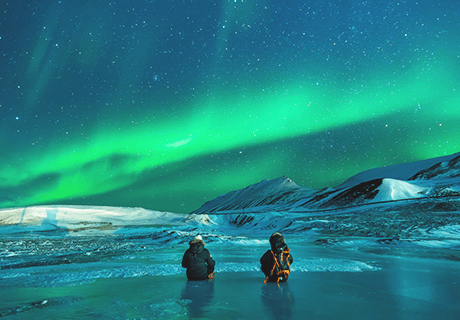 two people fishing near snow covered hills looking at the Northern Lights