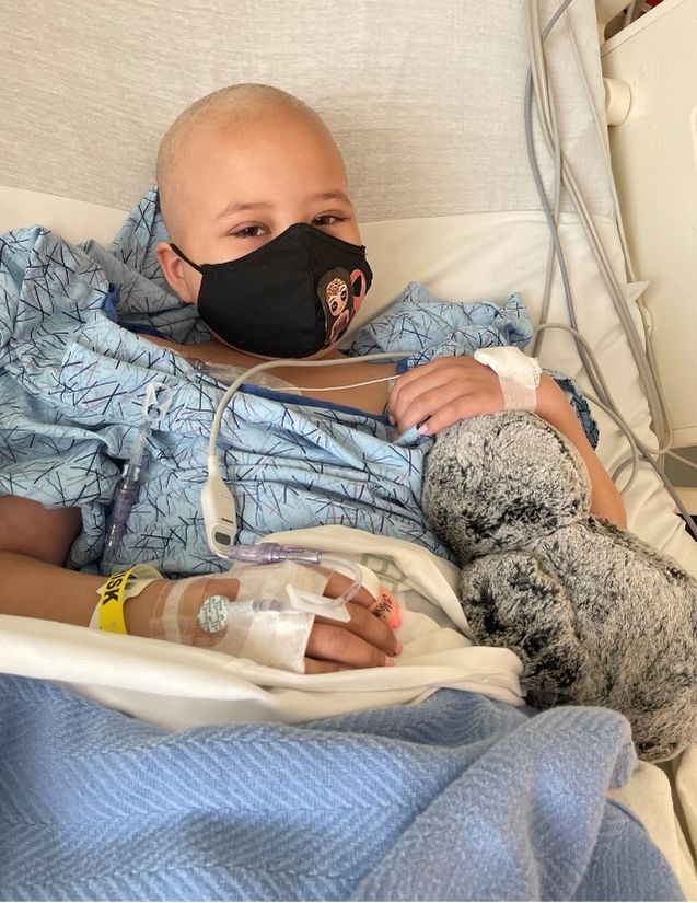 Pediatric stroke survivor Olivia Story on a hospital bed with tubes and wearing a mask 
