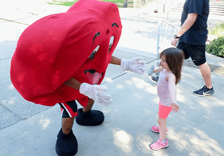 man in AHA ticker heart costume high fiving a young girl