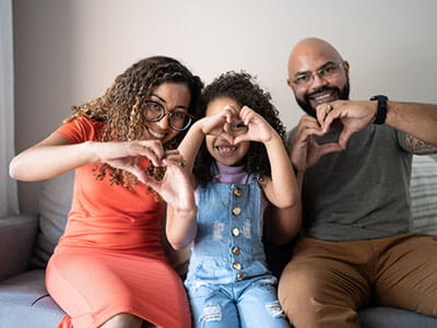 family sitting on the couch doing heart-shape with their hands